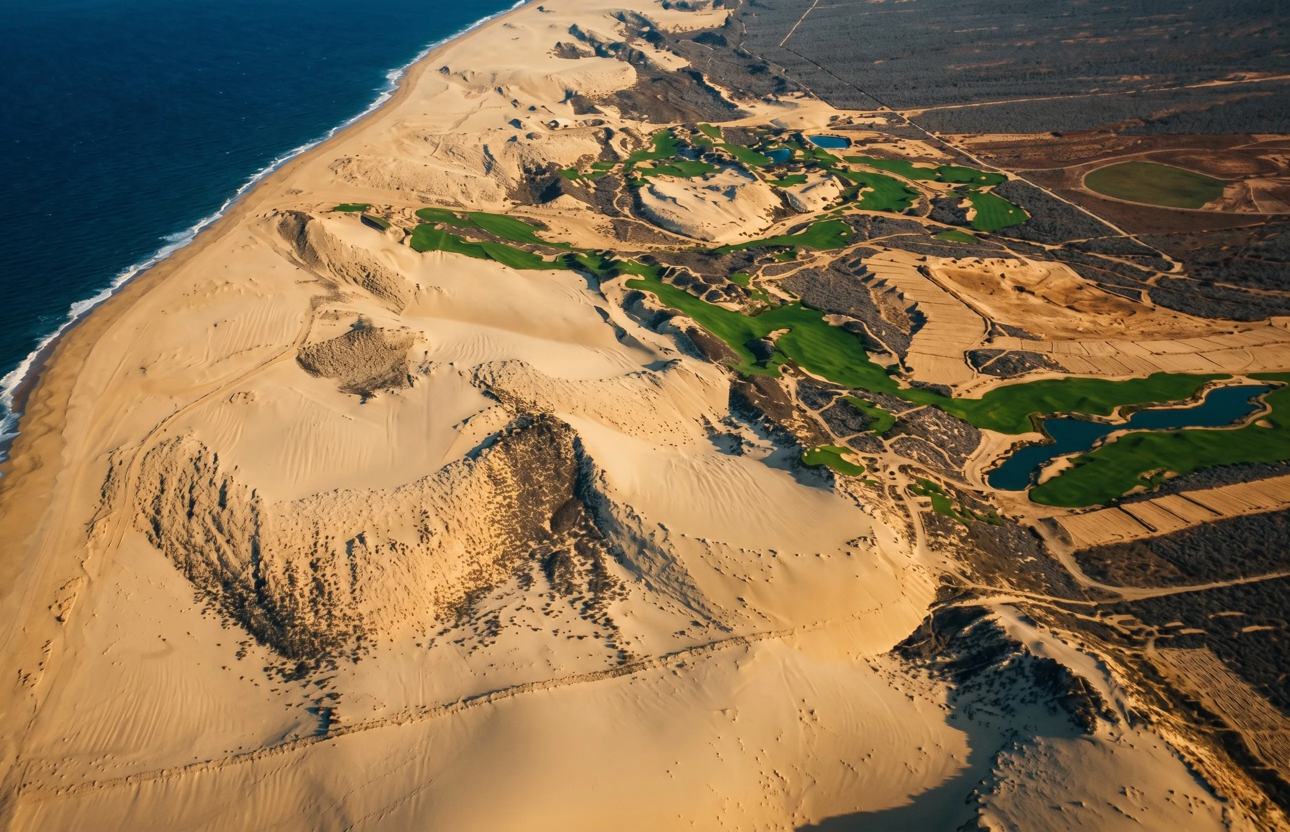 Dramatic panoramic aerial perspective of the championship Dunes Golf Course rolling through coastal sand dunes along the Pacific Ocean in Diamante Cabo San Lucas.