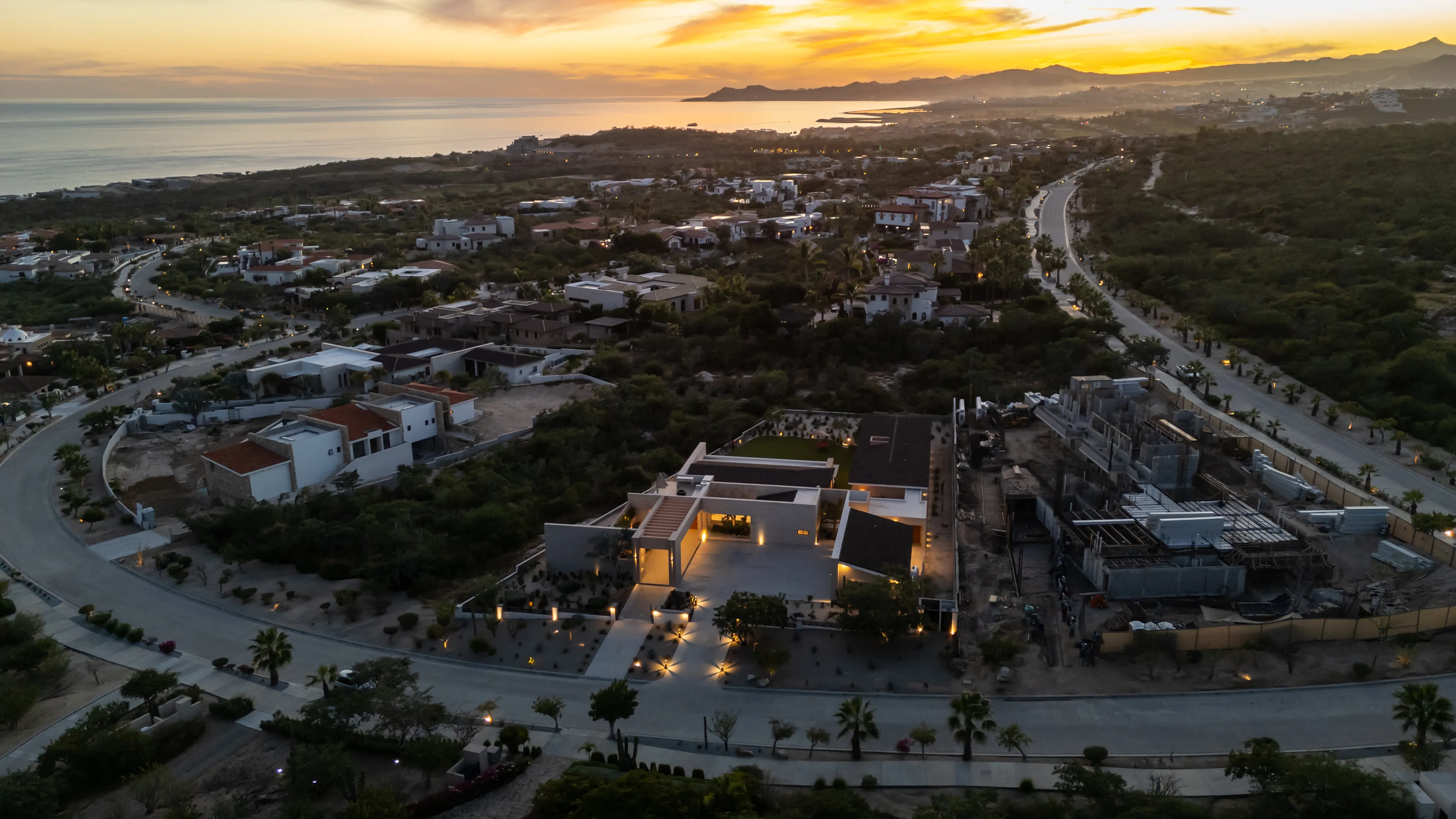 Aerial twilight perspective of luxury custom estates and illuminated streets within the Fundadores residential enclave in Puerto Los Cabos.