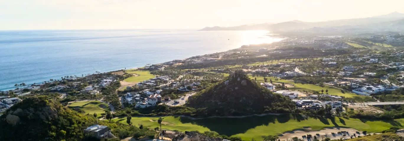 Wide aerial panoramic landscape showing the intersection of signature golf courses and luxury real estate enclaves in Puerto Los Cabos.