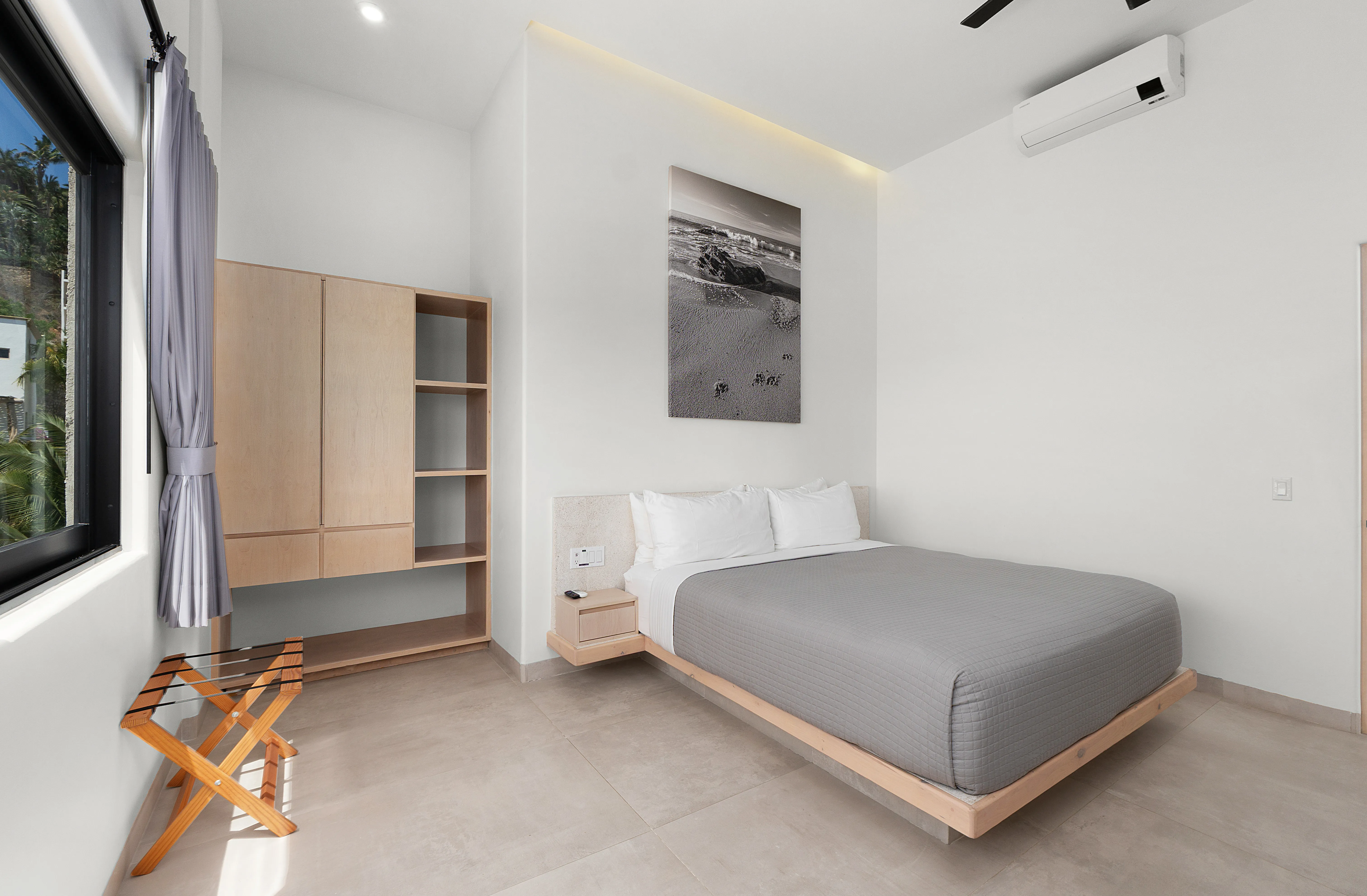 Modern luxury condominium bedroom featuring a custom wood wardrobe, coastal beach artwork, and palm tree views.