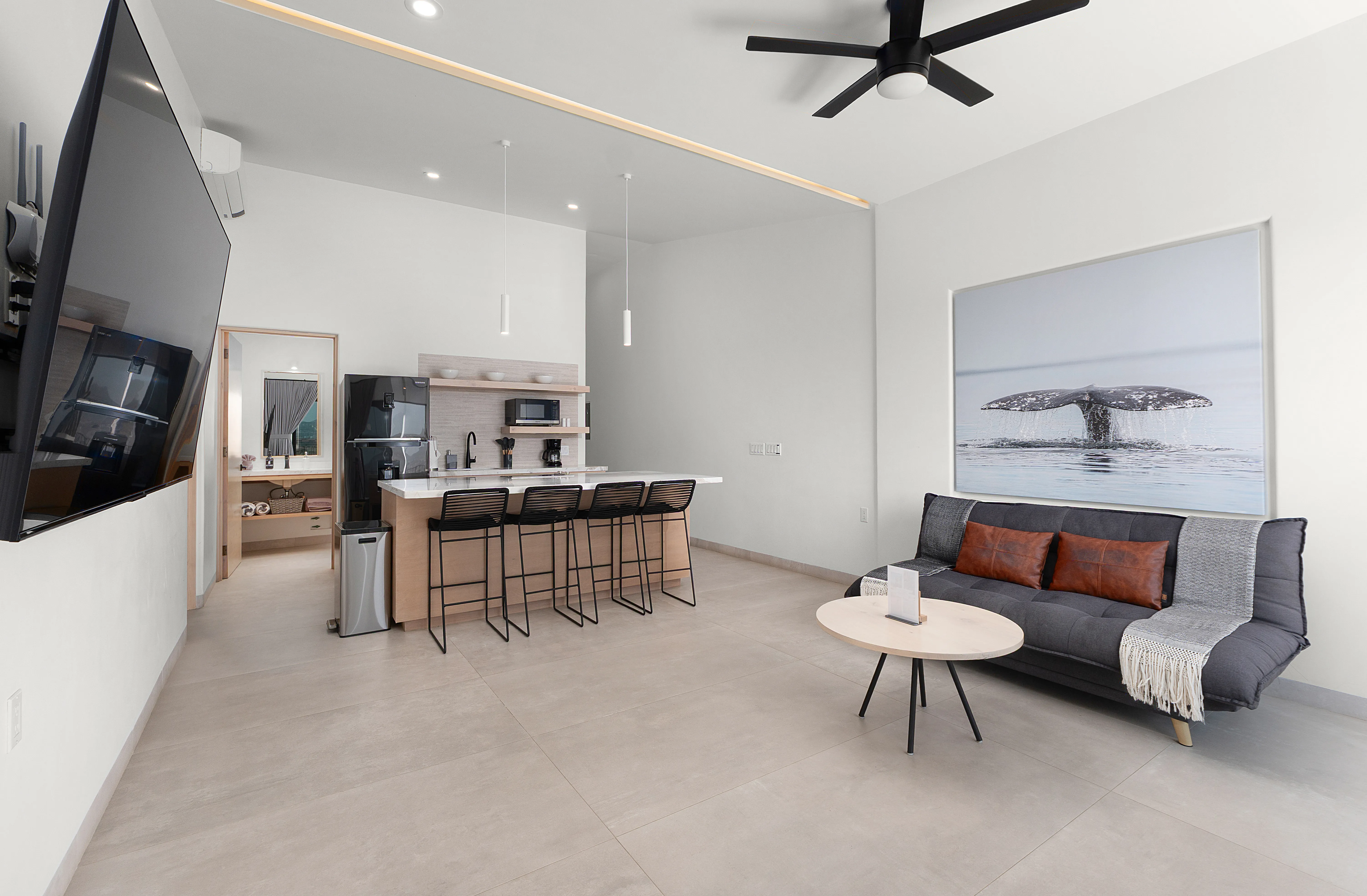 Contemporary integrated living and kitchen space featuring a large marble counter island, sleek bar stools, and custom art.