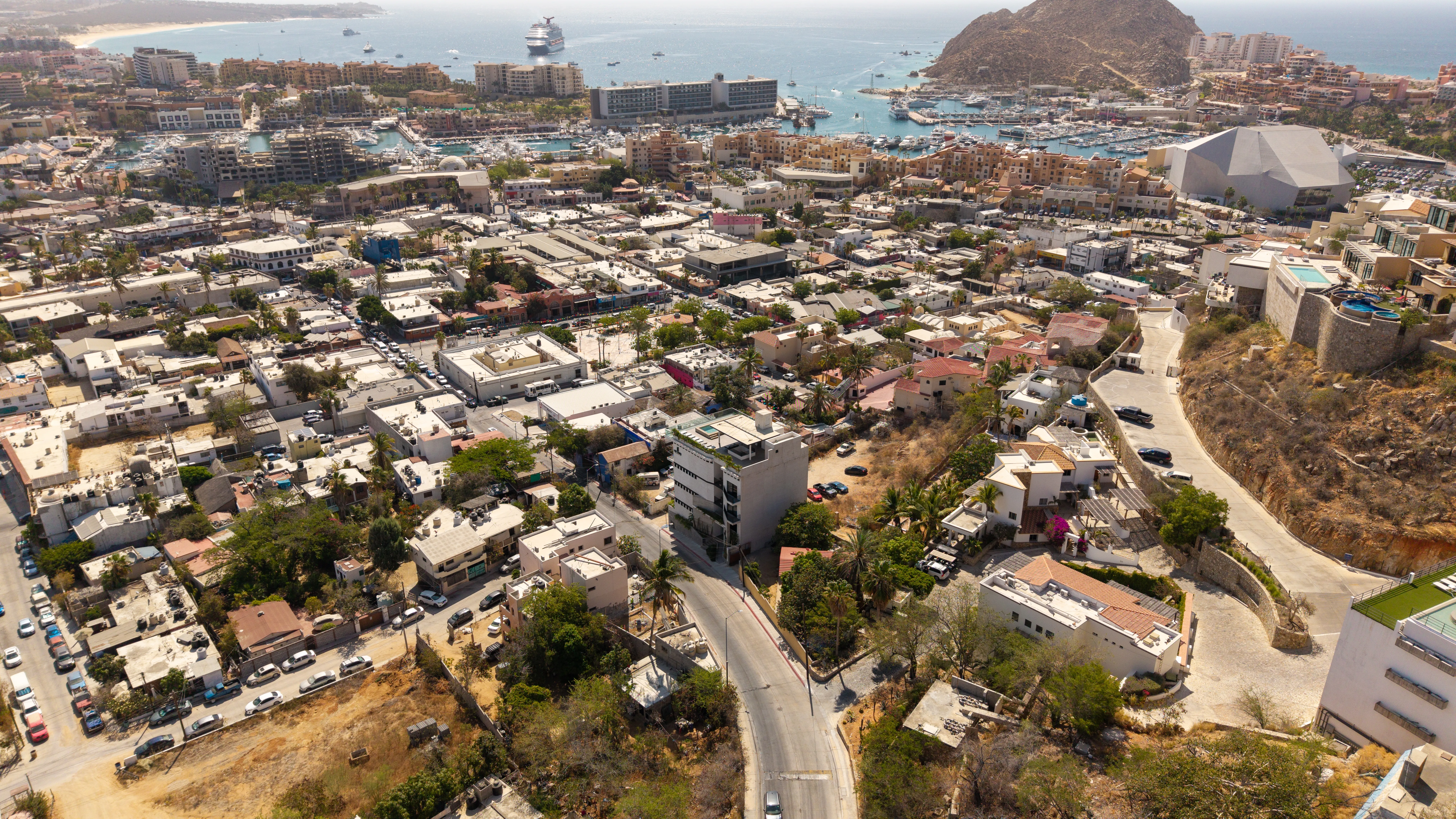 Elevated neighborhood overview displaying downtown Cabo San Lucas, the marina harbor, cruise ships, and El Arco backdrop.