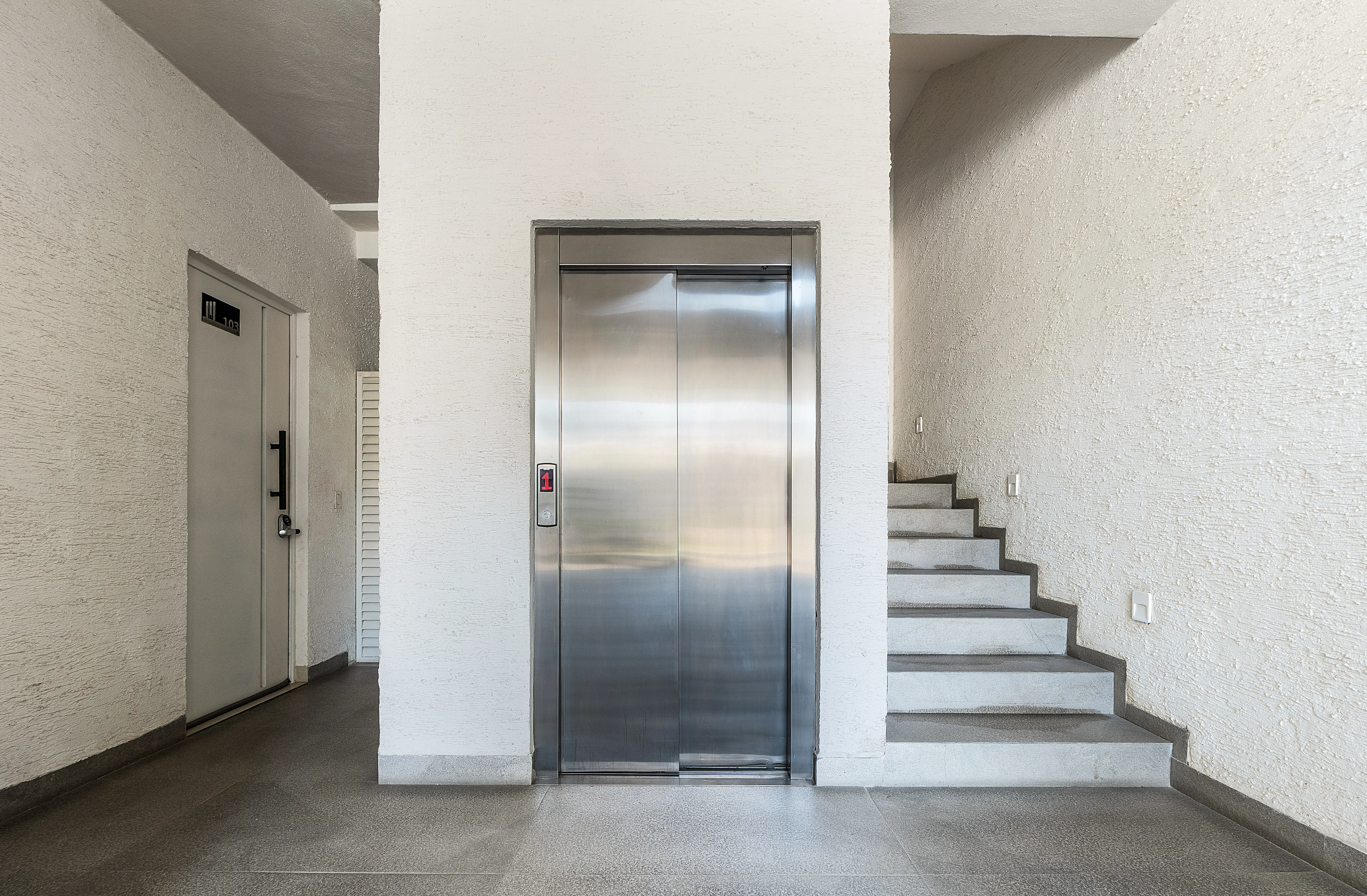 Architectural common area showcasing the secure elevator lobby, building stairwell, and pristine contemporary finishes.