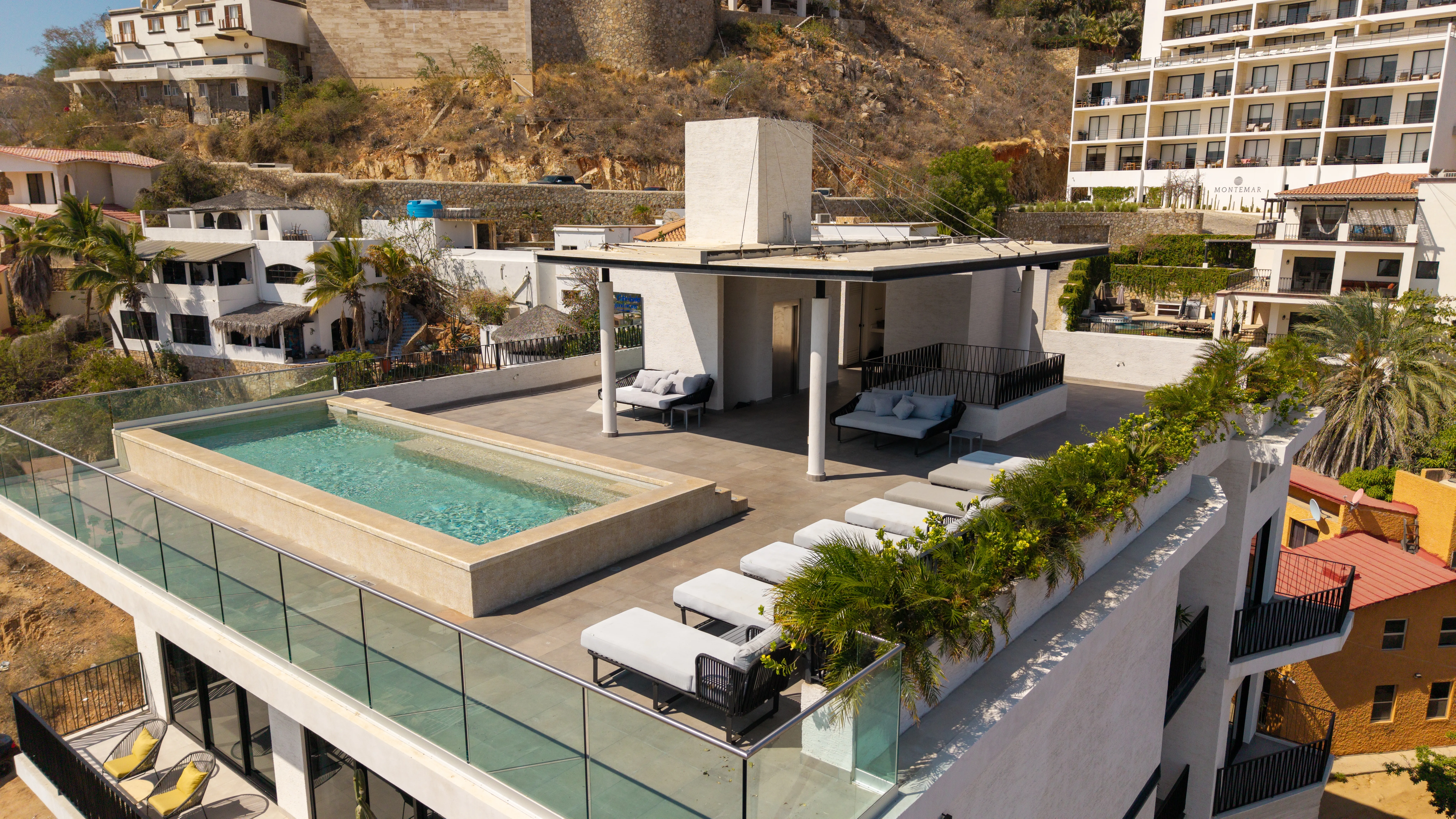 Rooftop terrace amenity area featuring private pergola daybeds, modern glass railings, and sweeping mountain views.