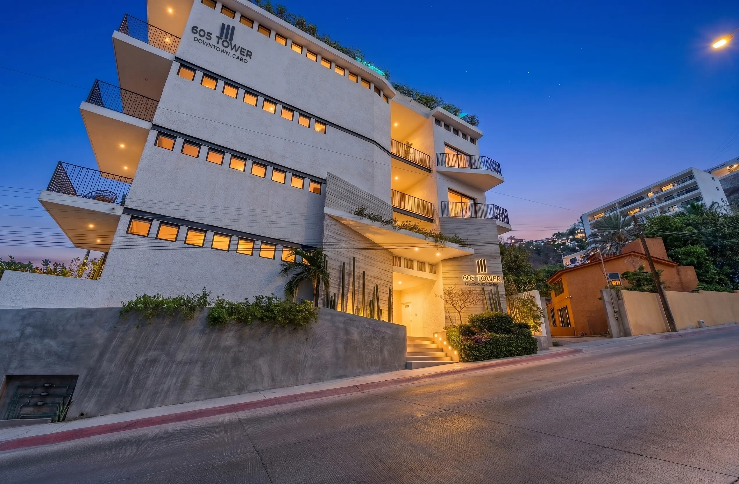 Sleek front entrance and exterior modern architectural facade of 605 Tower downtown studio apartments featuring contemporary balconies during blue hour.
