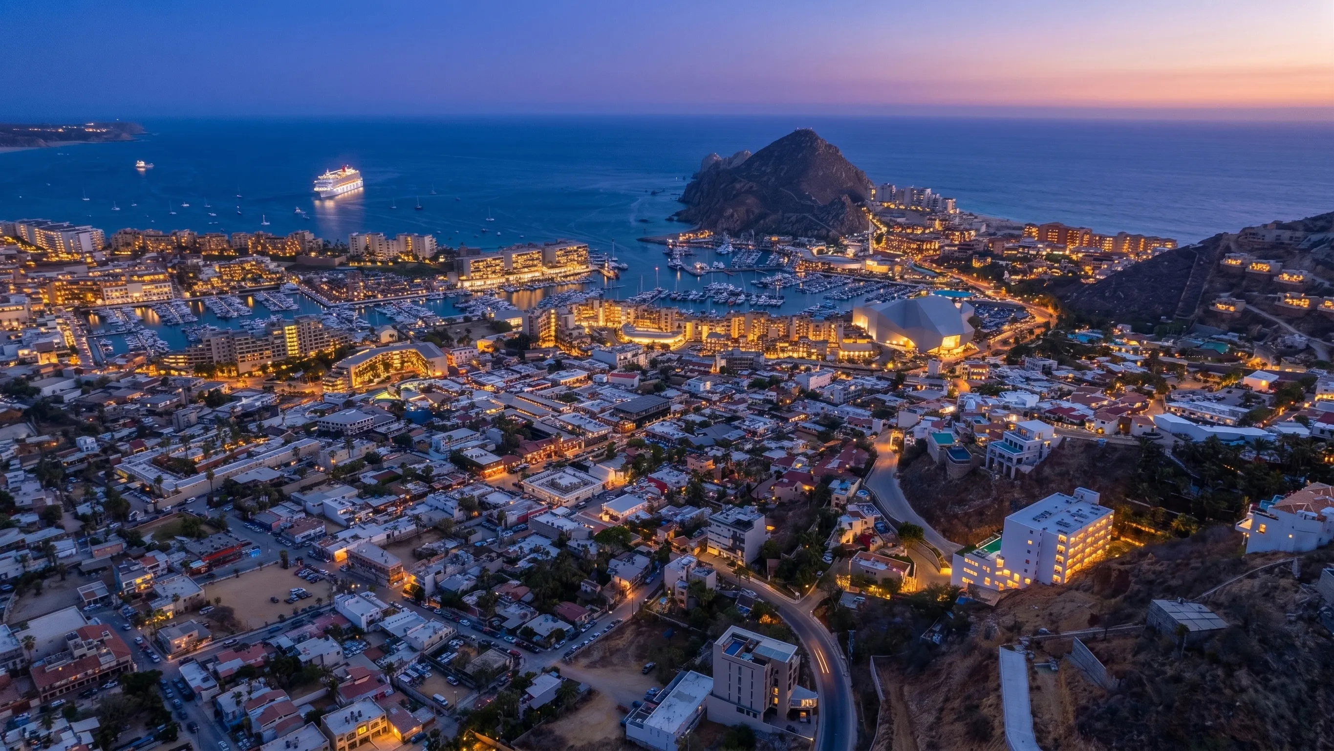 Stunning blue hour aerial coastal overview of the downtown Cabo San Lucas city grid, yacht port, and El Arco landmark from 605 Tower.