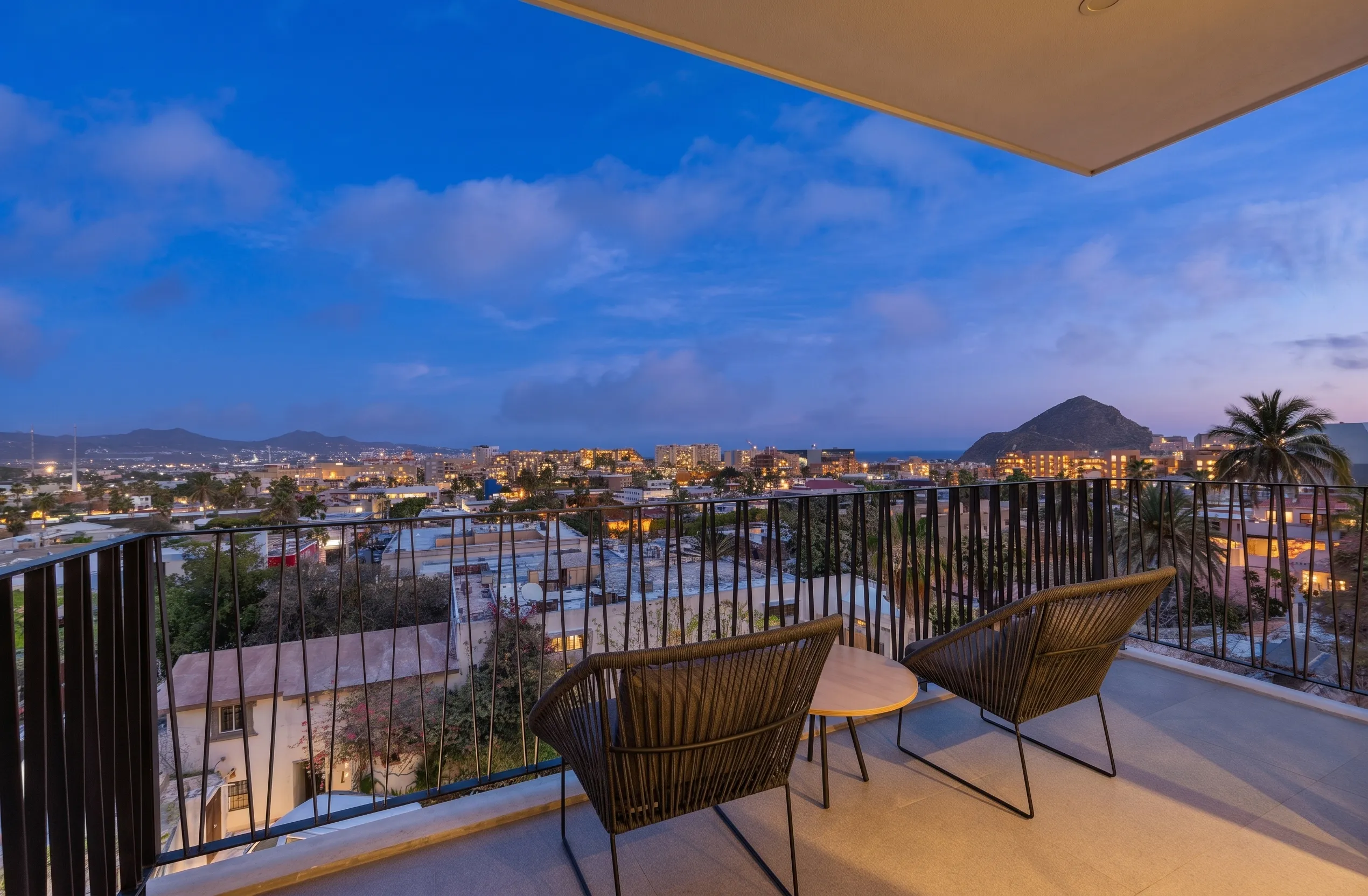 Cozy private studio unit balcony at 605 Tower featuring stylish Acapulco chairs and scenic twilight views of El Arco and downtown Cabo San Lucas.