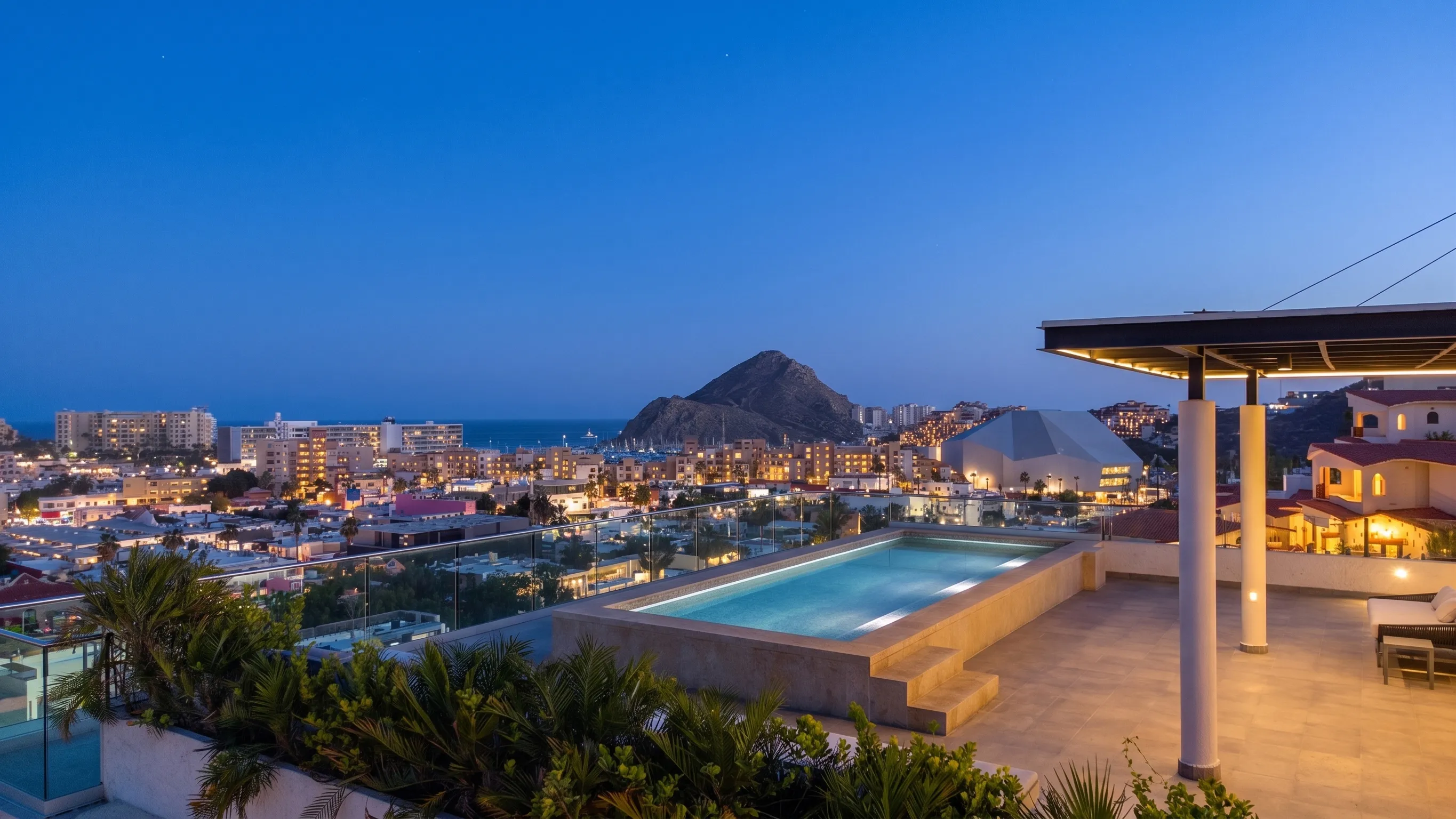 Luxury rooftop infinity pool under a shaded pergola lounge structure boasting panoramic twilight views of El Arco and the Cabo Marina from 605 Tower.