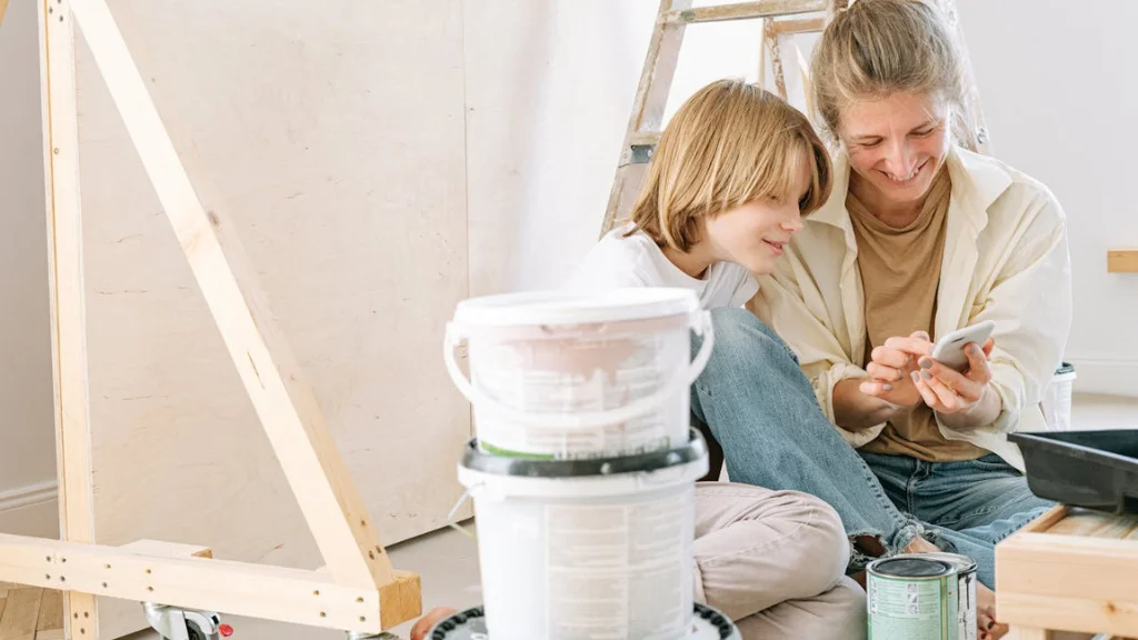 Woman and child looking at cell phone in a room with a ladder and paint cans